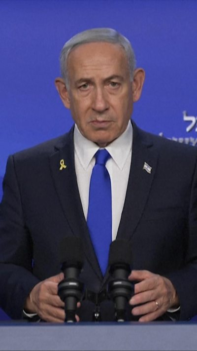 Benjamin Netanyahu speaks behind a podium while looking into a camera.
