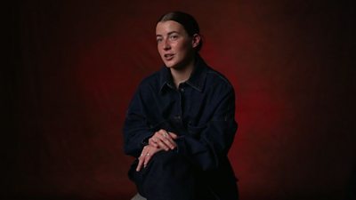 A portrait photograph of Angharad James. The background is a dark red colour