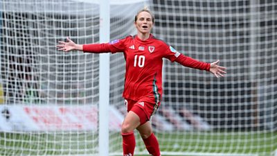 Jess Fishlock in Wales football kit with her arms stretched out to her sides running past a goal