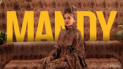 Diane Morgan in character as Mandy. She wears a leopard-print outfit, sitting on a leopard-print sofa, in front of leopard-print wallpaper. “Mandy†is written in large, yellow letters in the background.