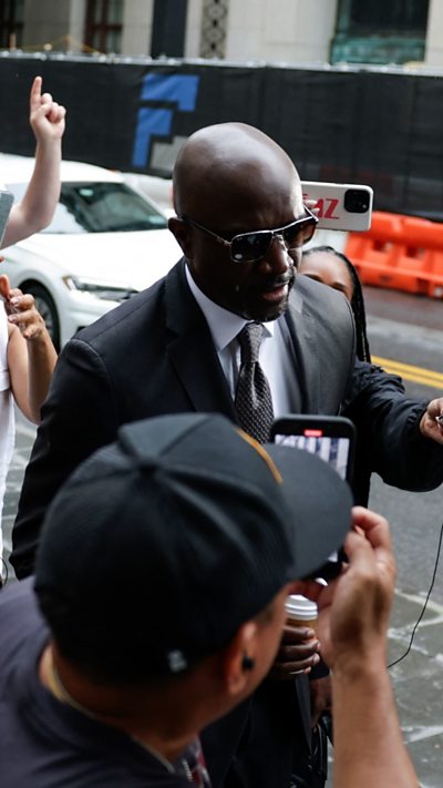 A man is walking being followed and surrounded by press