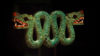 A turquoise double-headed serpent covered with a mosaic of turquoise and red thorny oyster shell, posing with their mouths open baring their teeth against a black background