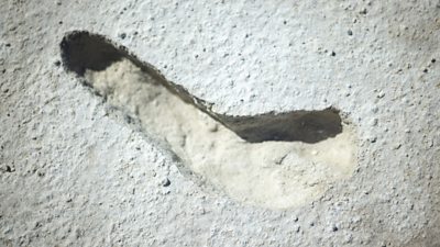 A footprint, but not like a modern day footprint, on some white sand. There are no toe prints visible.