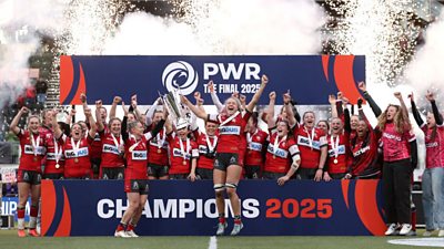 the Gloucester-Hartpury team celebrating winning the 2025 final. They're all cheering while someone holds the trophy up and fireworks in the background