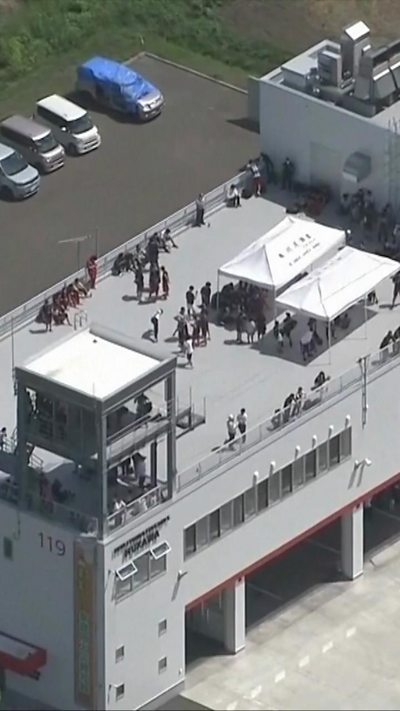 People shelter on the roof of a grey boxy building.
