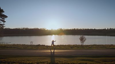 A lone figure stands in front of a body of water, imitating boxing moves as the sun casts a shadow.
