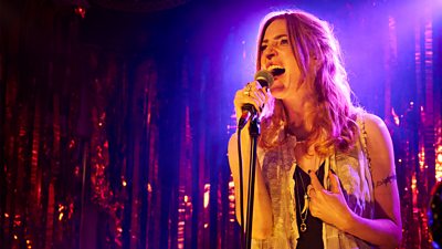 A woman stands on stage and sings into a microphone. 