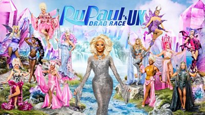 RuPaul surrounded by the Queens of 2025. They are on the banks each side of a river and Ru is in the middle of the shot with a waterfall behind him. Everyone is in glamorous, showstopper outfits.