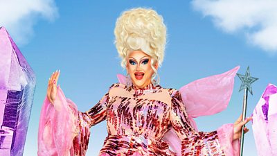 A drag queen wearing pink against a blue sky holding a fairy wand
