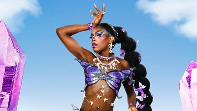 A drag queen wearing purple bralette shaped like a butterfly against a blue sky