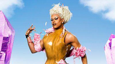 A drag queen wearing pink and brown outfit with feathers against a blue sky