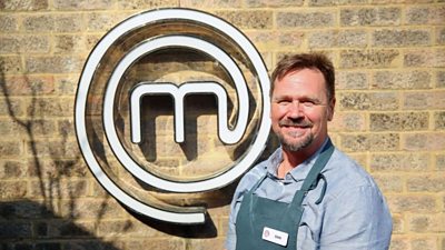 A portrait image of a contestant stood against an exposed brick wall, with the MasterChef logo behind him.