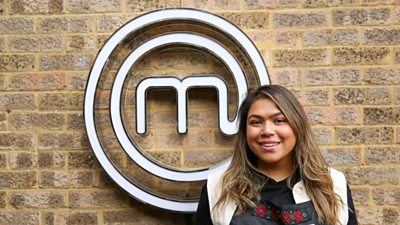 A portrait image of a contestant stood against an exposed brick wall, with the MasterChef circular white logo behind her.