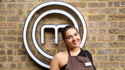 A portrait image of a contestant stood against an exposed brick wall, with the MasterChef circular white logo behind her.
