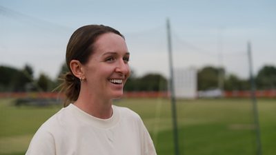 Kate Cross stands on a cricket pitch smiling