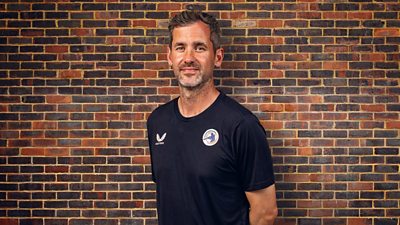 Kyle Hogg is pictured in front of a brick wall with his arms behind his back