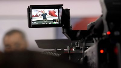 A close up shot of a video camera viewfinder, showing Marc in the ѿý News studio presenting to camera.