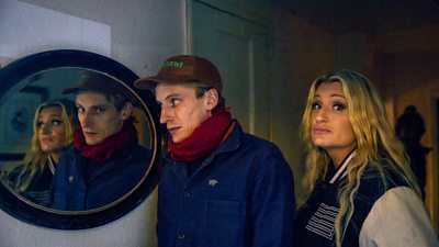 Daisy May and Charlie Cooper stood in a dark hallway with a round mirror on the wall
