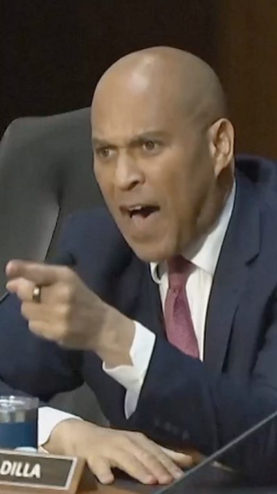 Senator Cory Booker points his finger and shouts toward the witness seat from a large dias in a US Senate hearing room.
