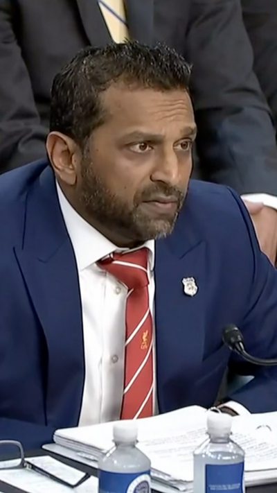 Kash Patel sits behind a table during a US Senate hearing with water bottles and a large binder in front of him.