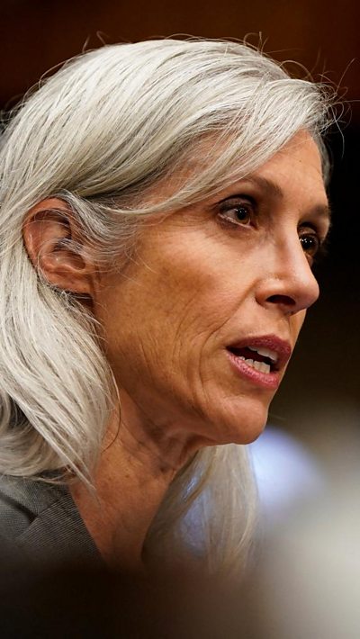 A woman speaks toward a Senate dias with silver, grey hair.