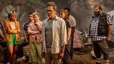 Seven plane crash survivors looking down at something on the jungle floor.