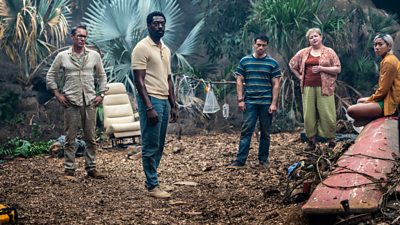 Five of the plane crash survivors looking at the camera in a jungle setting. A plane seat is in the image away from the wreckage.