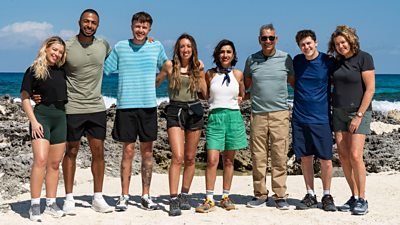 A group of people stand together arm in arm on a beach