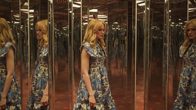  Emma Laird stood in a hall of mirrors wearing a floral blue and white tea-dress - her reflection duplicated over and over