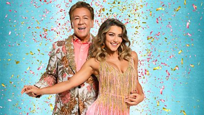 Ross wears a light floral patterned suit and peach shirt while Jowita wears a peachy pink and gold fringe trimmed dress