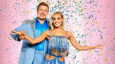 Thomas wears a blue slik shirt beneath a light blue suit, trimmed with sparkles. Amy wears a blue and silver fringe trimmed top and skirt with cutout detail.