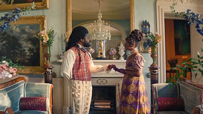A man in period clothing taking a woman in period clothing's hand. Their surroundings are inside a period building and very ornate room filled with flowers in tall vases and art on the walls..
