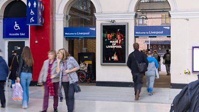 Made in Liverpool artwork on a wall at a busy train station. There are people going about their day walking past it.