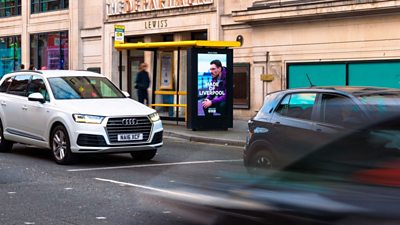 Made in Liverpool artwork on the side of a bus shelter on a busy street in Liverpool's city centre. Cars are passing.