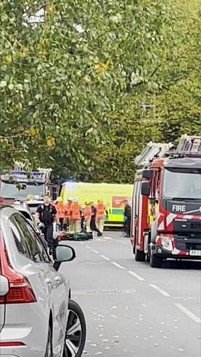 A fire engine, an ambulance and emergency service workers on a tree-lined street