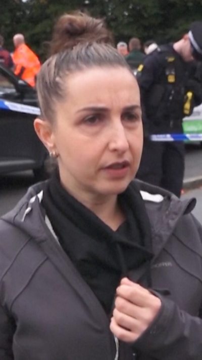 A woman in black stands in front of a police officer near police tape in the street