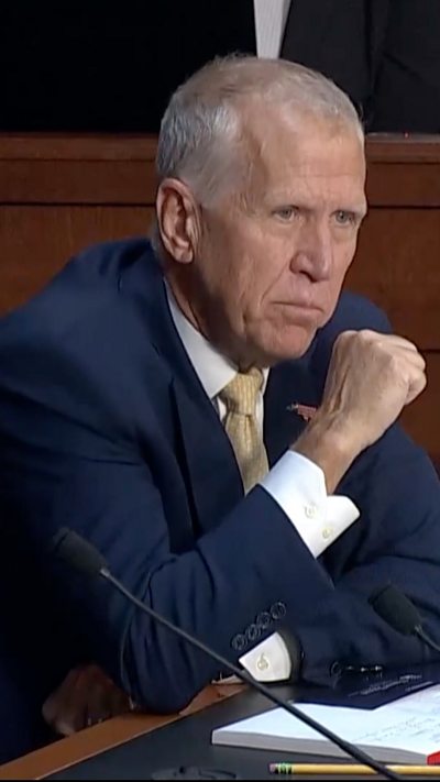 Vertical frame of Thom Tillis holding his fist clenched, in a blue suit and yellow tie.