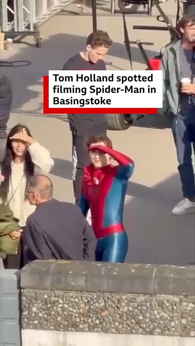 Tom Holland in his Spider-Man outfit shielding his eyes from the sun.