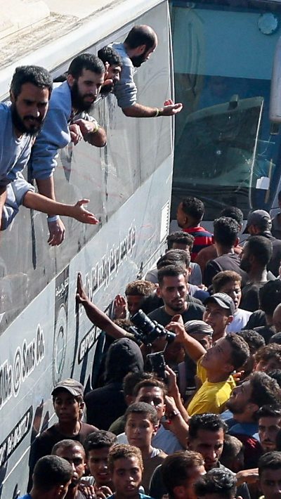 Palestinian prisoners lean out of a bus window. Many people on the ground look up at them