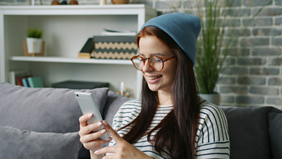 A person is smiling while using a mobile phone in a living room.