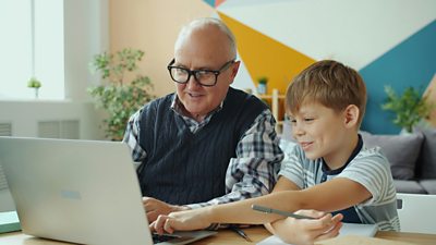A grandparent sitting with a child at a laptop as they look at something together that is on the screen.