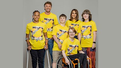 A group of four young people and two presenters pose against a grey background wearing yellow Pudsey Rules t-shirts. One Challenge Squad member uses crutches and the other sits in a wheelchair.