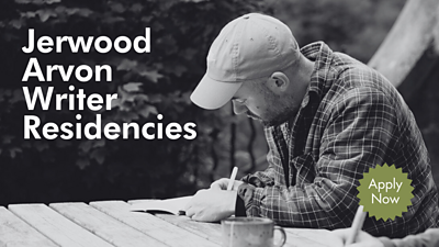 Black-and-white photo of a person in a cap and checkered jacket writing in a notebook at an outdoor wooden table, with a mug in front. Text reads “Jerwood Arvon Writer Residencies” and a green badge says “Apply Now.”