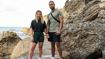 A man and a woman stand on rocks holding hands