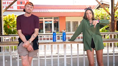 A man and a woman lean against a railing. She gestures a thumbs down.
