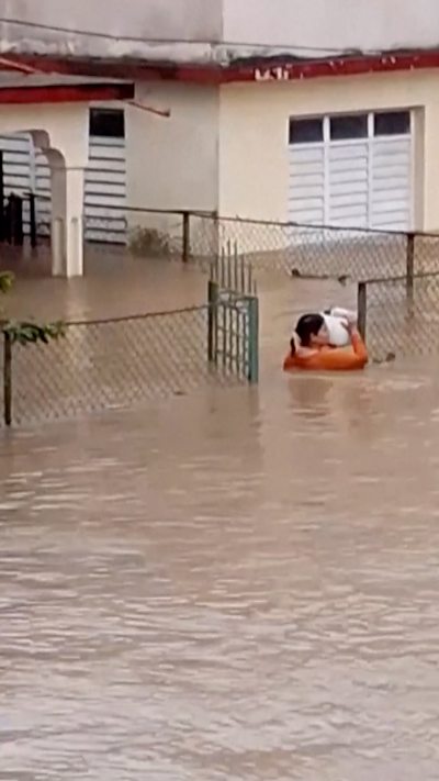 Woman in Cuba is seen carrying a bucket home with the water up to her shoulders.