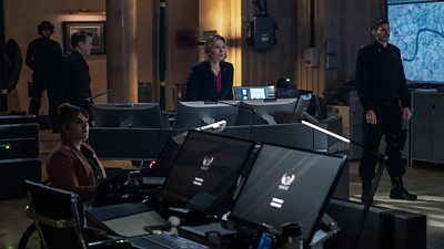 A group of people sit and stand behind computers looking concerned