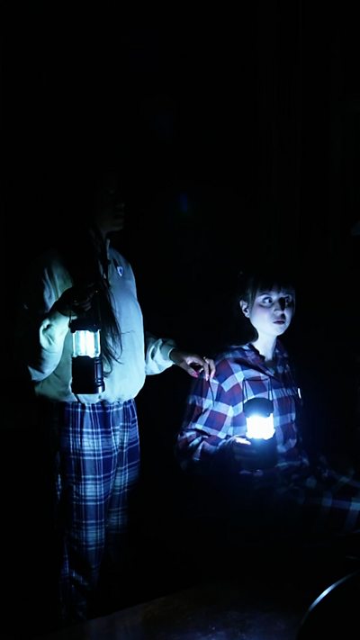 Abby and Shini dimly lit in a haunted library.
