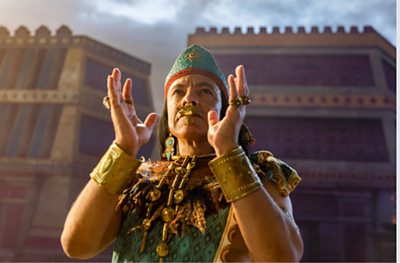 A man dressed in Aztec clothing looks as though he is about to clap. 