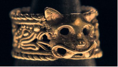 A close-up of a gold ring, shaped like a jaguar cat 